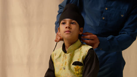 Studio-Shot-Of-Father-Tying-Turban-Onto-Head-Of-Young-Sikh-Son-Wearing-Traditional-Waistcoat-As-Sequence-Part-2-Of-10